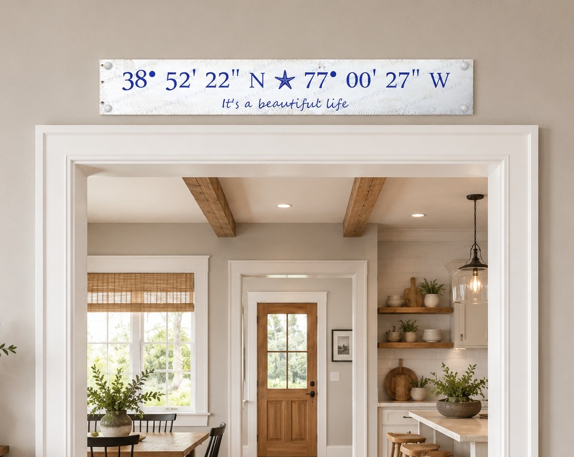 A 30″ × 4.5″ frosted acrylic Coordinate Board mounted with silver stand-offs on a cream wall — navy coordinates 38° 58′ 03″ N, anchor symbol, 76° 17′ 53″ W with 'home sweet home' in script below.
